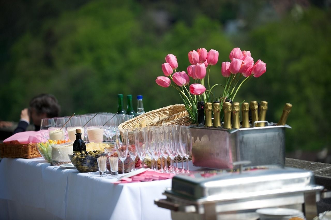 Una mesa de buffet con diversos alimentos, una botella y un jarrón con tulipanes rosados.