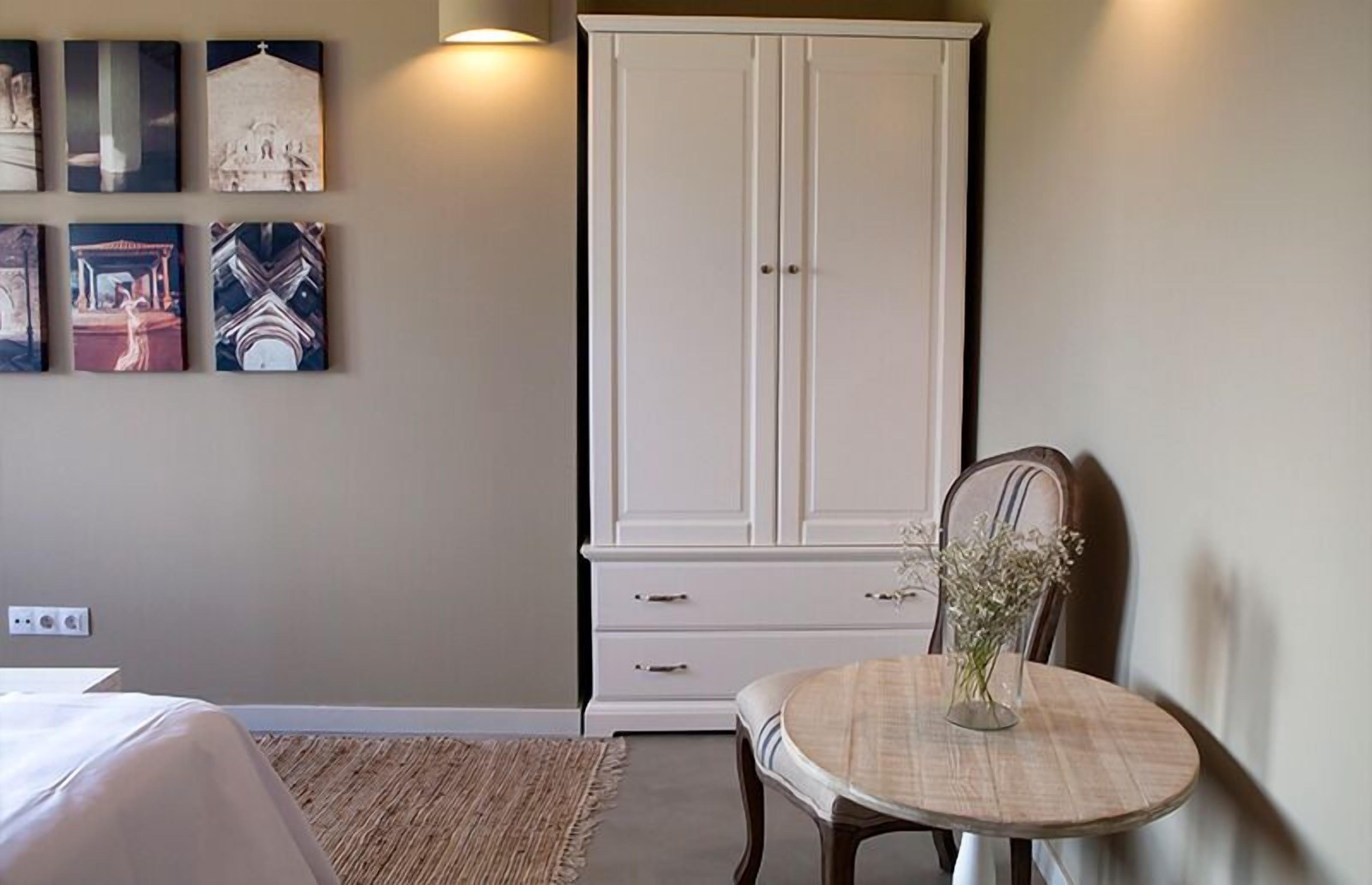 A bedroom with a bed, a wardrobe, a dining table with a vase, and artwork on the wall.