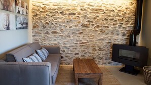A living room with a stone wall, a sofa, a wooden coffee table, and a flat-screen TV. - Hotel Mas de Cebrián (Puertomingalvo)