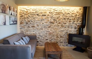Una sala de estar con pared de piedra, un sofá, una mesa de centro de madera y un televisor de pantalla plana.