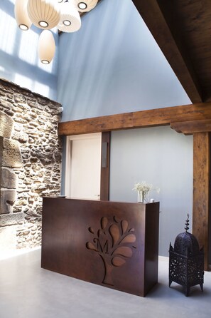 A reception desk with a tree design, a stone wall, a wooden ceiling, and a lantern. - Hotel Mas de Cebrián (Puertomingalvo)