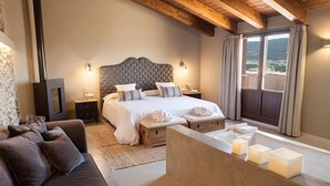 A bedroom with a large bed, bedside tables, a wooden bench, and a view of the outdoors through a window. - Hotel Mas de Cebrián (Puertomingalvo)
