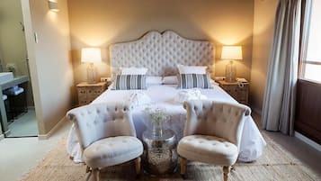 Een ruime slaapkamer met een groot bed, twee nachtkastjes met lampen en twee fauteuils.