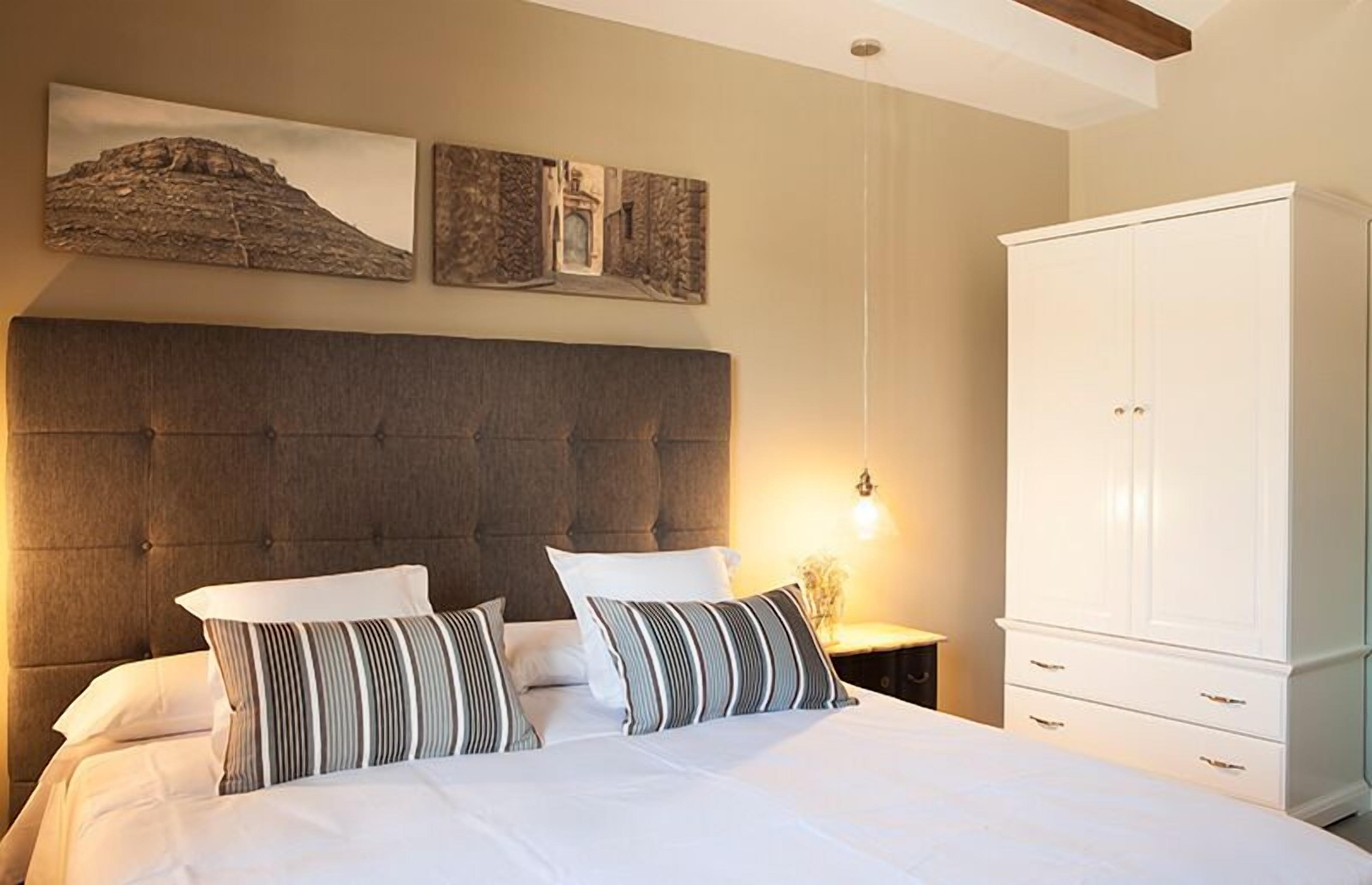 Un dormitorio con una cama grande, cabecera de madera, un armario blanco y dos obras de arte colgadas en la pared.