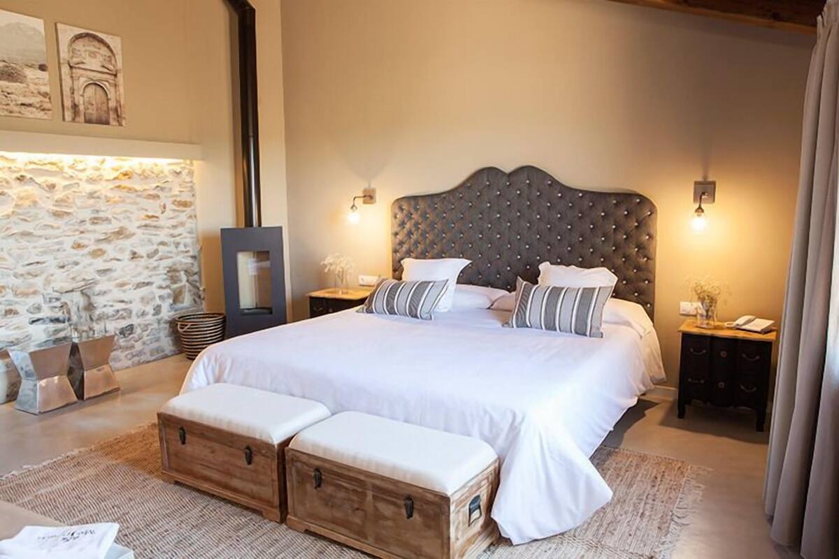 A bedroom with a large bed, wooden headboard, two bedside tables, and a stone wall.