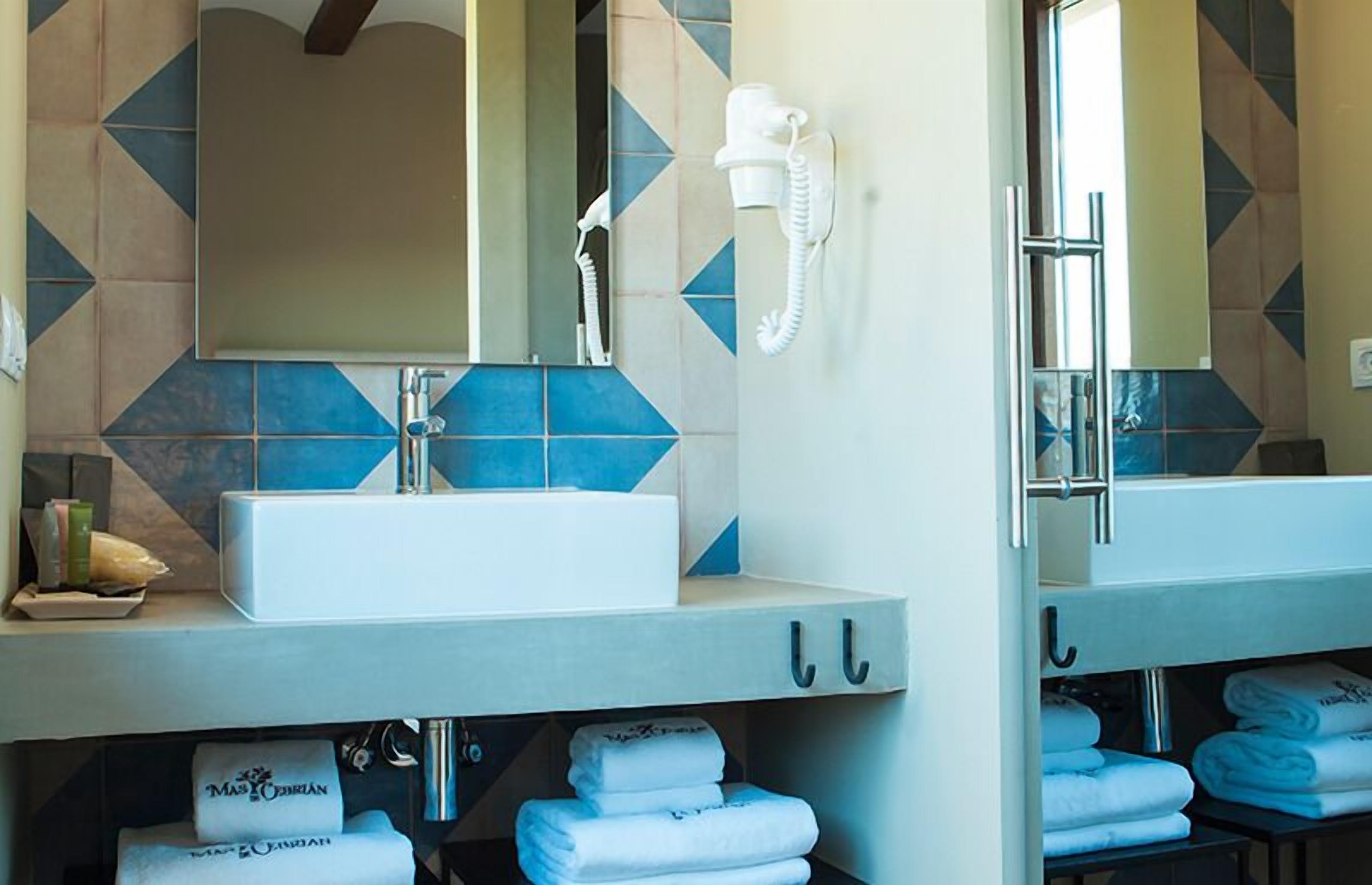 A bathroom with a large mirror, a sink, and a hairdryer. There are towels and a bottle on the counter.