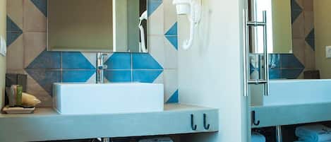 A bathroom with a large mirror, a sink, and a hairdryer. There are towels and a bottle on the counter.