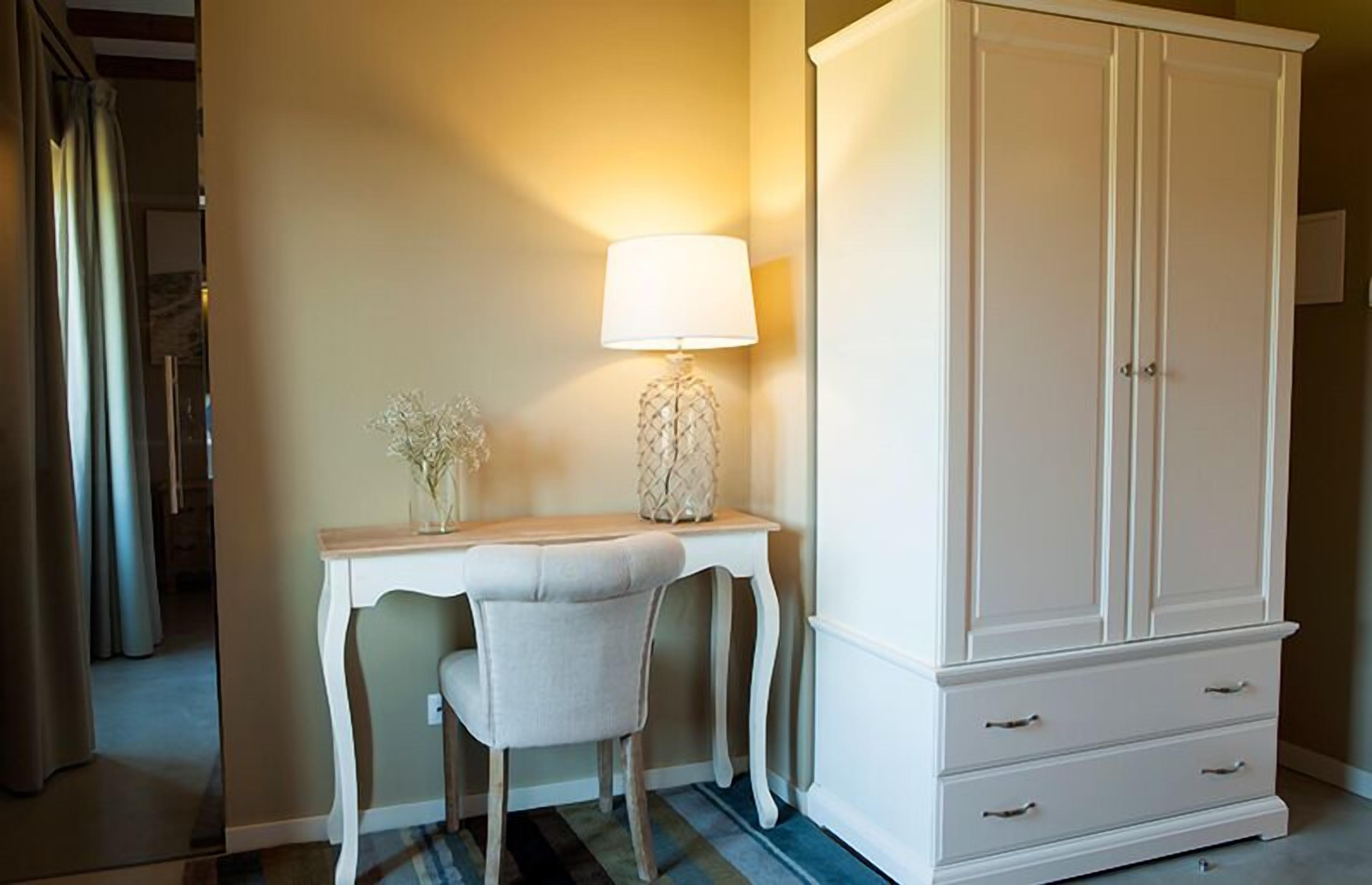 A room with a white desk, a chair, a lamp, and a large white wardrobe.