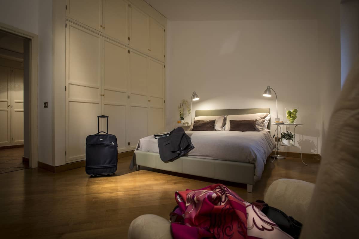 Une chambre à coucher avec un lit, une valise, une chaise, une table de chevet et une armoire.
