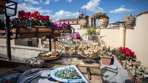 A rooftop terrace with potted plants, a table with food and drinks, and a magazine. - Dimora Torremuzza (Palermo)