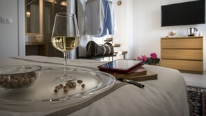 A neatly made bed with a glass tray holding nuts and a glass of white wine, a book, and a pen on the bed. - Dimora Torremuzza (Palermo)