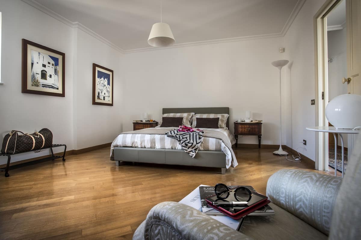 Une chambre à coucher avec un lit, des tables de chevet, une lampe et un banc.