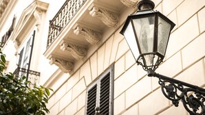 A street lamp attached to a building with ornate architectural details, including decorative moldings and a balcony with a wrought iron railing. - Dimora Torremuzza (Palermo)