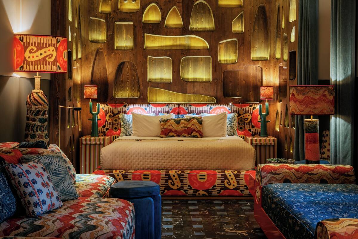 A hotel room with a large bed, two side tables, a sofa, and a patterned rug.