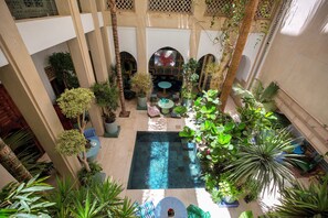 Un pati interior amb una piscina central, envoltat de plantes en testos i zones d'estar.
