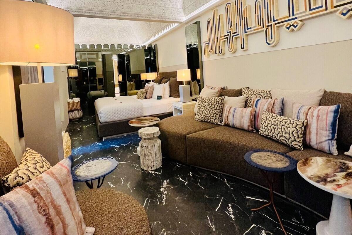 A modern hotel room with a marble floor, a large bed, a sofa, and a decorative wall piece.