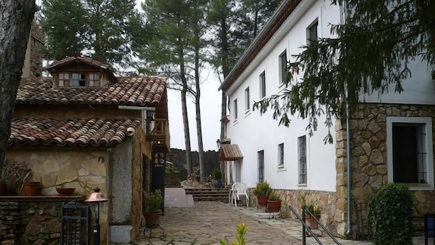 A stone pathway leading to a white building with a tiled roof and a stone wall. There are potted plants and a metal gate along the path. - Hotel Castillo de Uña (Una)