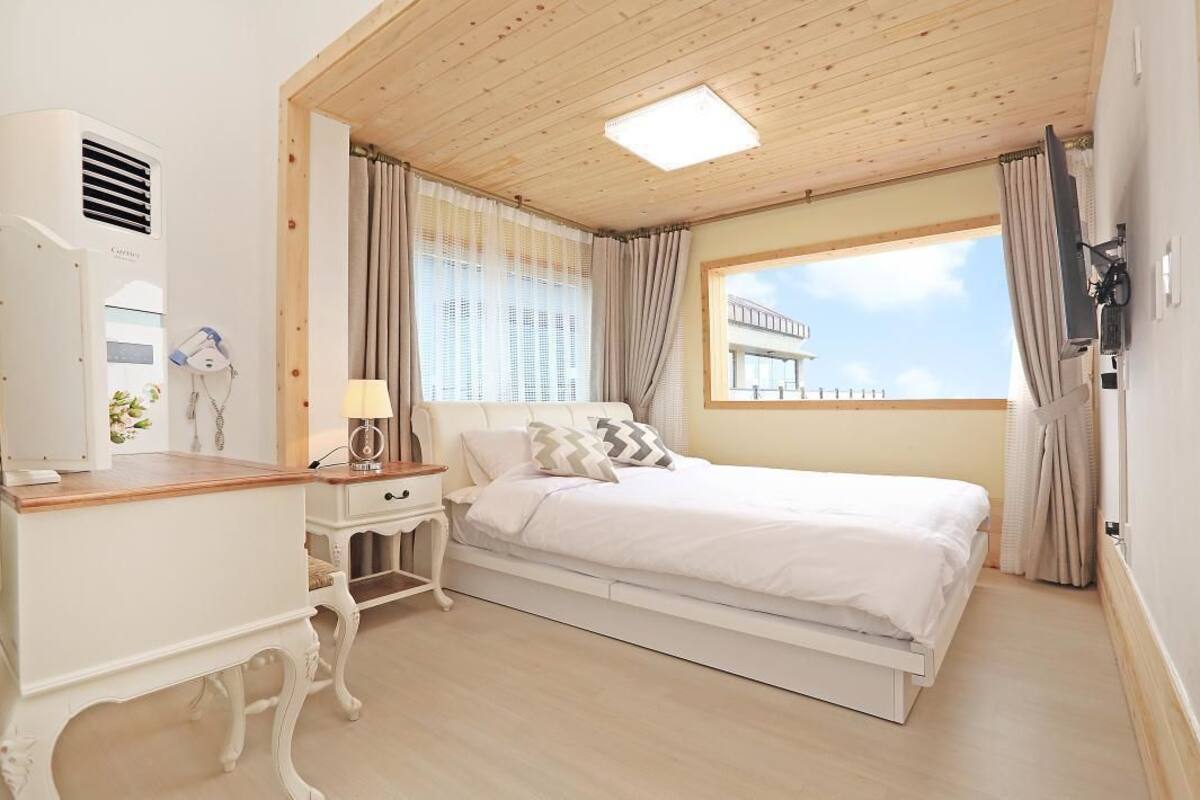 Une chambre à coucher avec un lit, une table de chevet, une lampe et une fenêtre avec des rideaux.