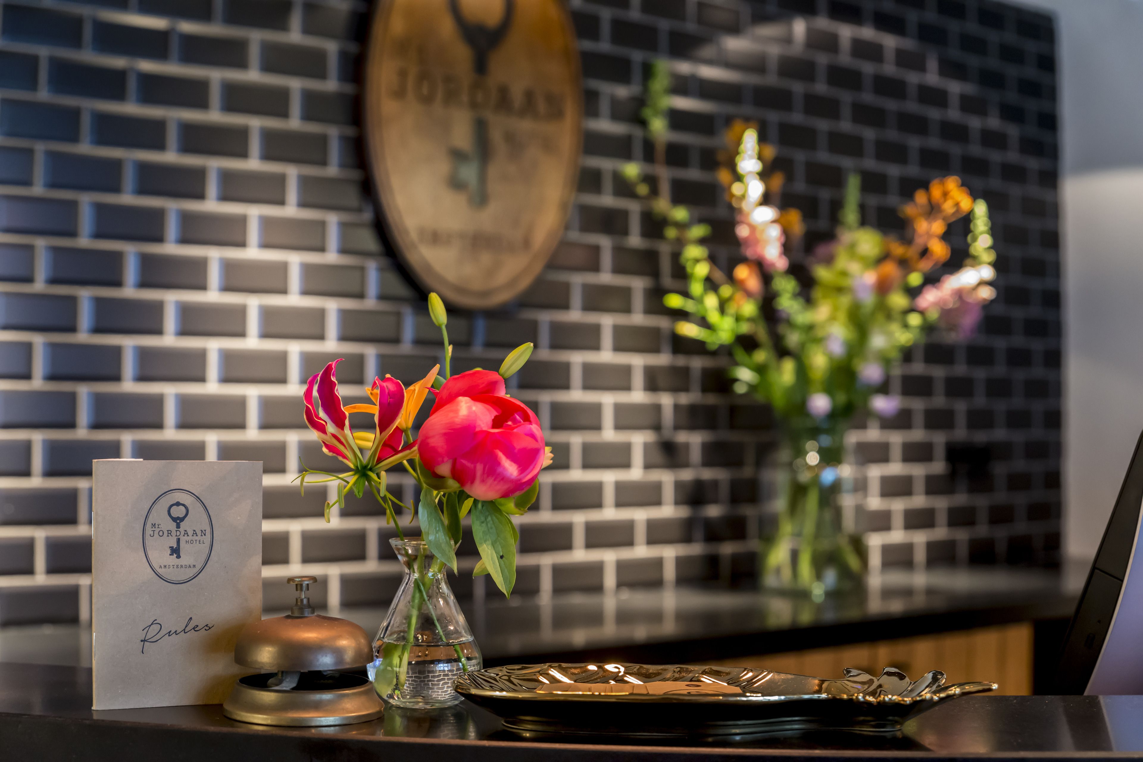 A reception desk with a wooden plaque, a glass vase with flowers, and a metal bell.
