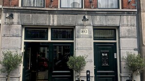 A building with two green doors, numbered 102, and a small tree in front of each door.