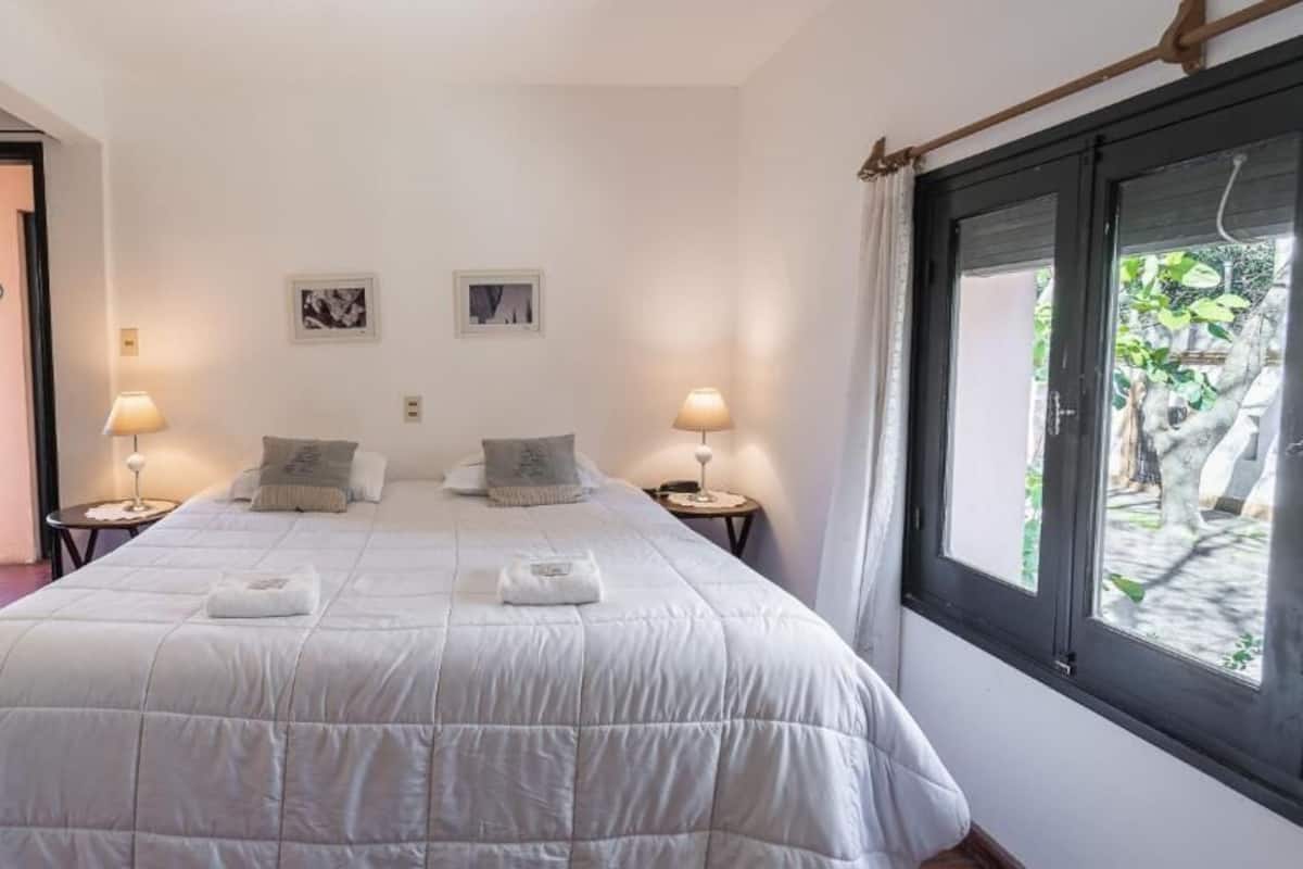 A bedroom with a large bed, two bedside tables with lamps, and a window with a view of greenery.