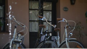 A row of bicycles parked in front of a building with a brown facade and a black door. - Posada de la Flor (Colonia del Sacramento)