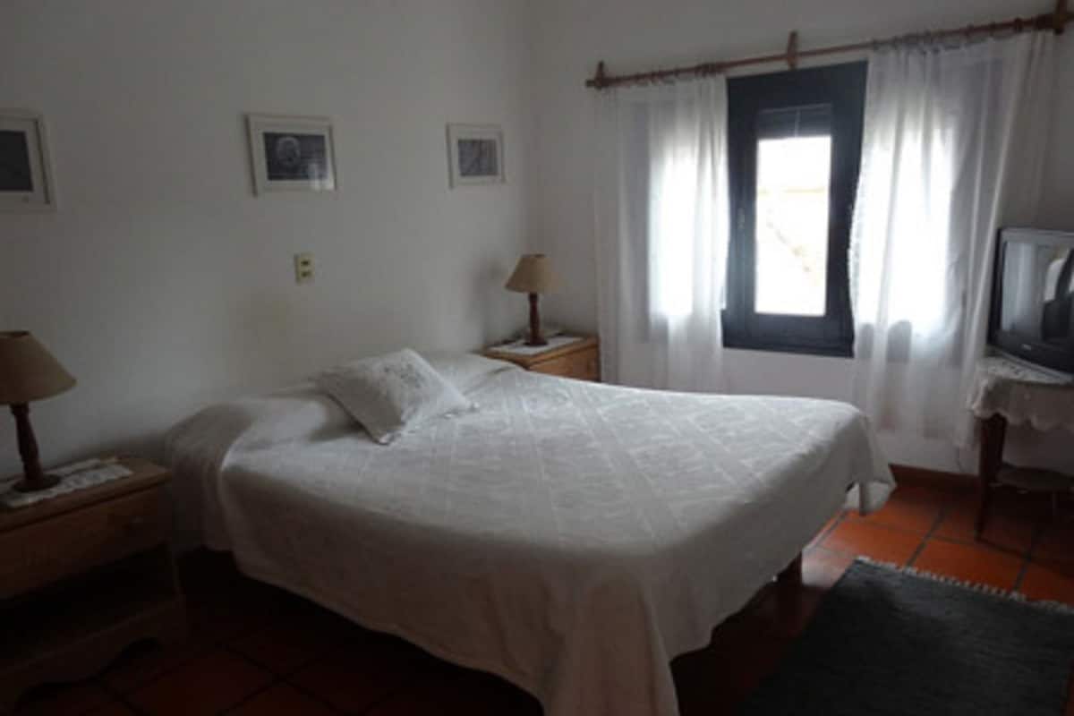 A bedroom with a bed, a nightstand, a lamp, a television, and a window with curtains.