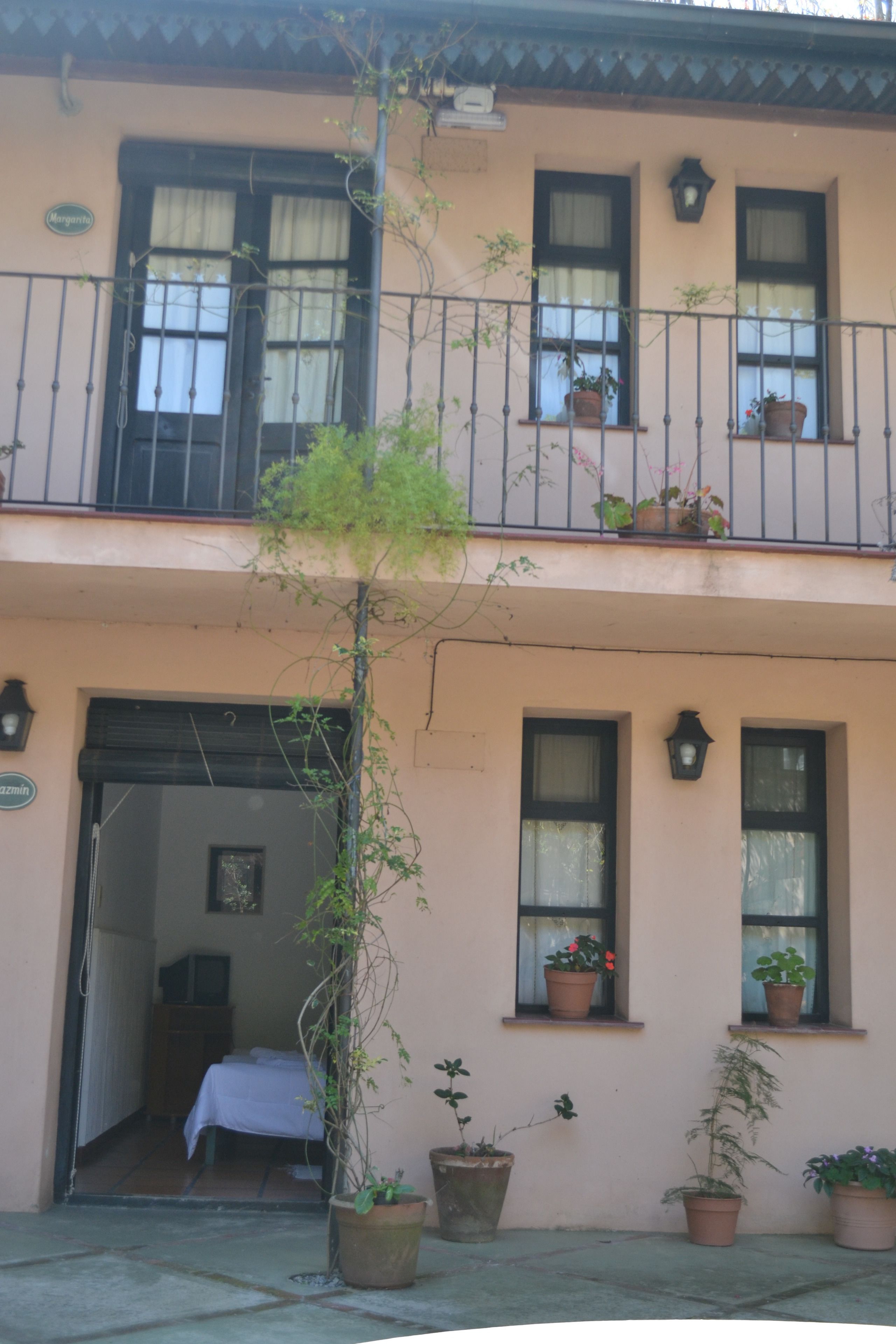 A two-story building with balconies, potted plants, and a visible entrance.