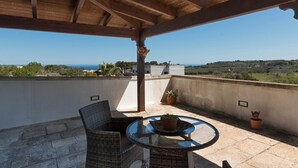 A covered outdoor area with wicker furniture, a glass table, and potted plants. - L'Agrumeto (Diso)