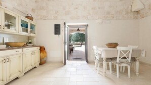 A kitchen with a stone floor, white cabinets, and a dining area with a table and chairs. - Le Site (Ostuni)