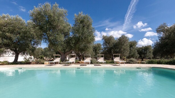 A swimming pool with lounge chairs and trees in the background. - Le Site (Ostuni)