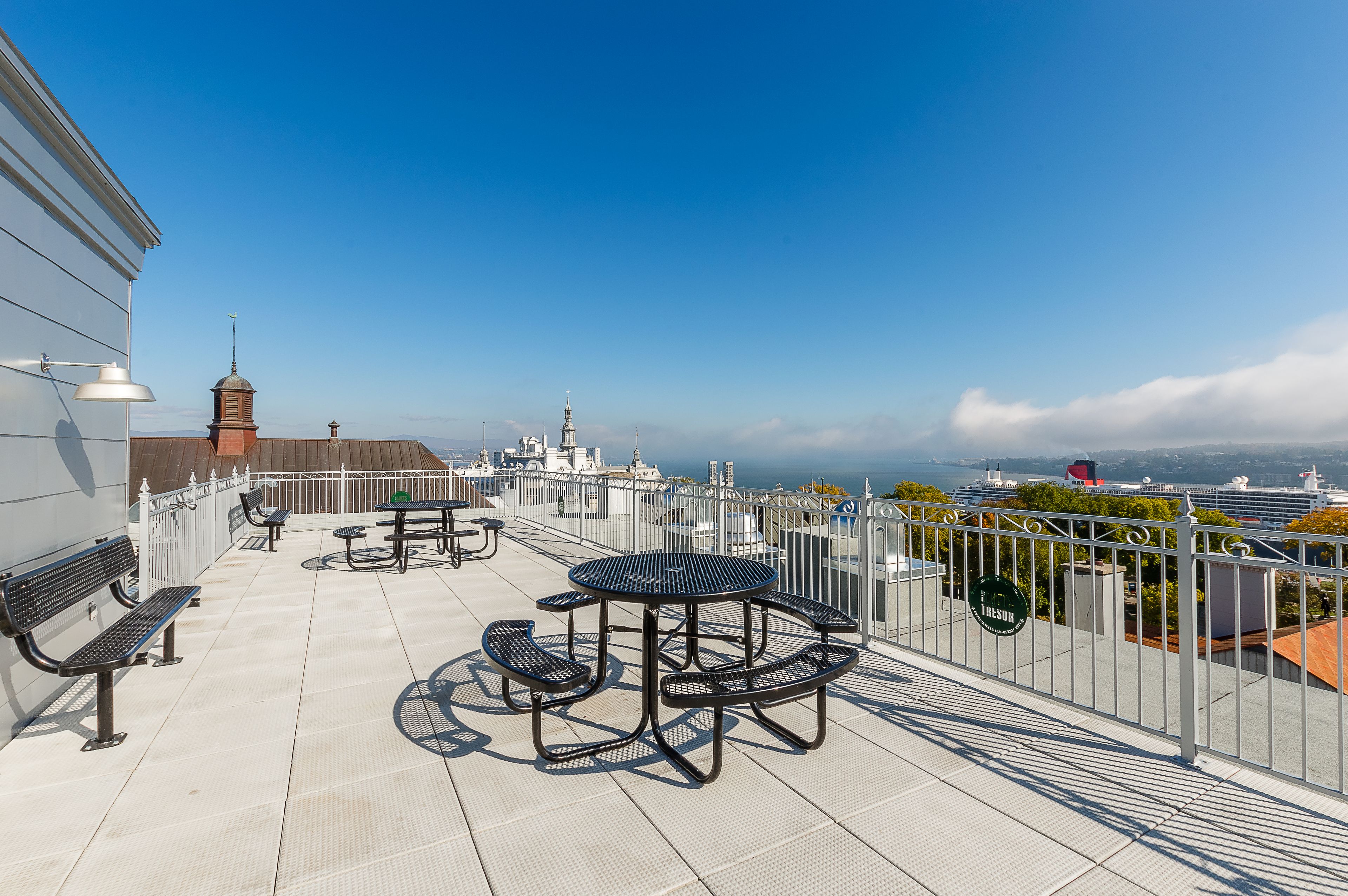 A rooftop terrace with picnic tables and benches, offering a view of the city and the ocean.
