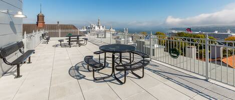 A rooftop terrace with picnic tables and benches, offering a view of the city and the ocean.