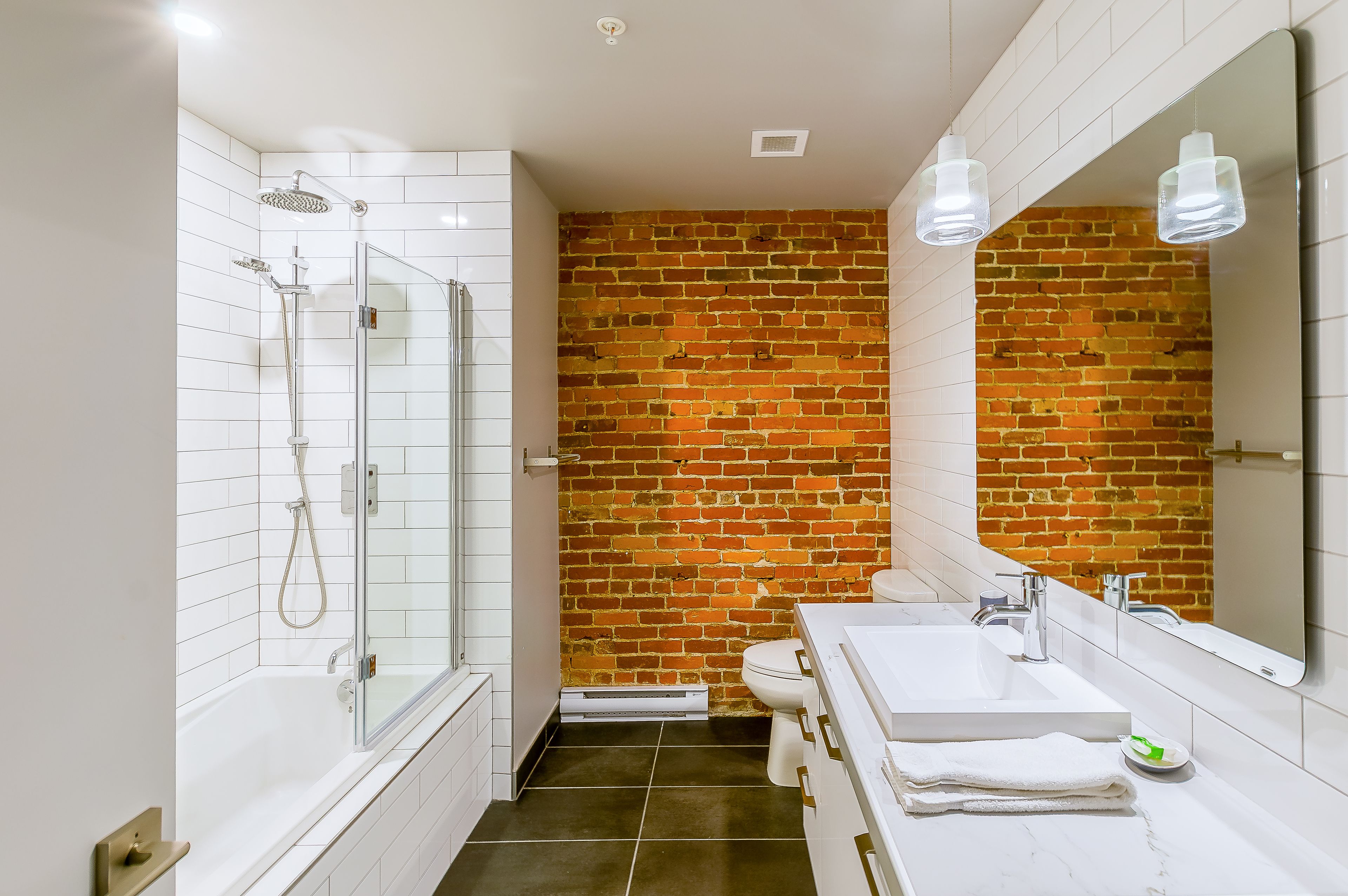 Ein modernes Badezimmer mit einer ein Glasfachwerk-Dusche, weißen Fliesen, einer Ziegelauslage, einem großen Spiegel und einem weißen Waschbecken mit Unterschrank.