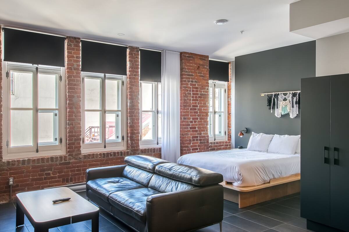 Ein modernes Zimmer mit Backsteinwand, einer Ledersofa, einem Bett und einem Kleiderschrank.