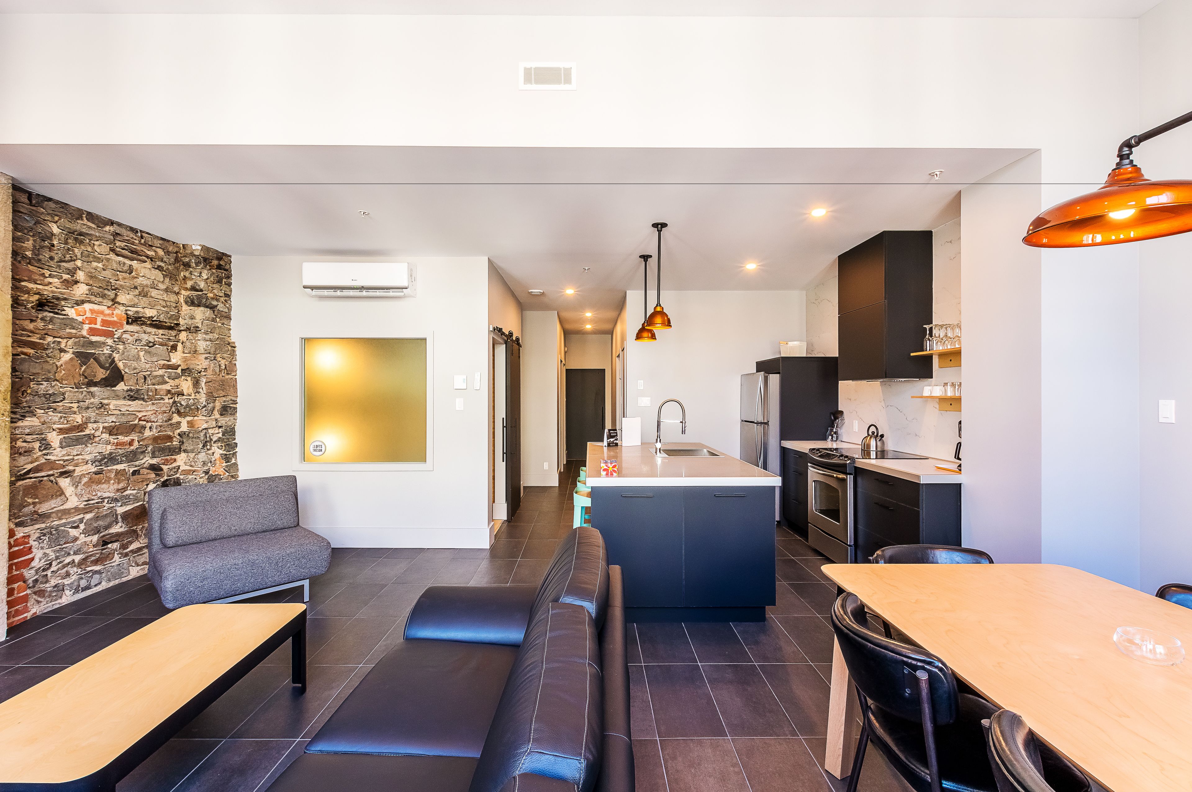 Una cocina moderna con una isla central, zona de comedor con banco y pared decorativa de piedra.