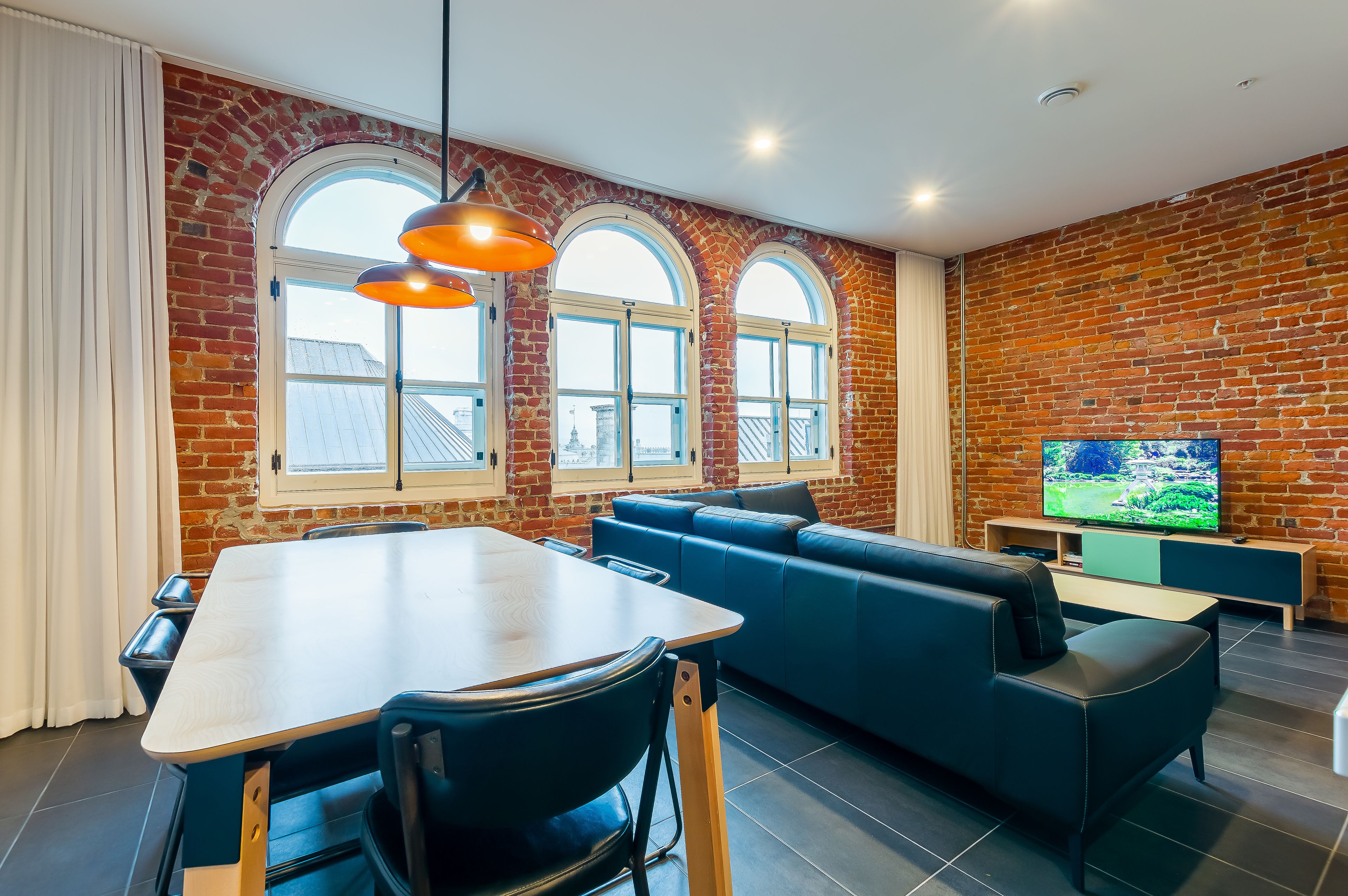 Una sala de estar moderna con pared de ladrillo, televisor grande, sofá y mesa de comedor.