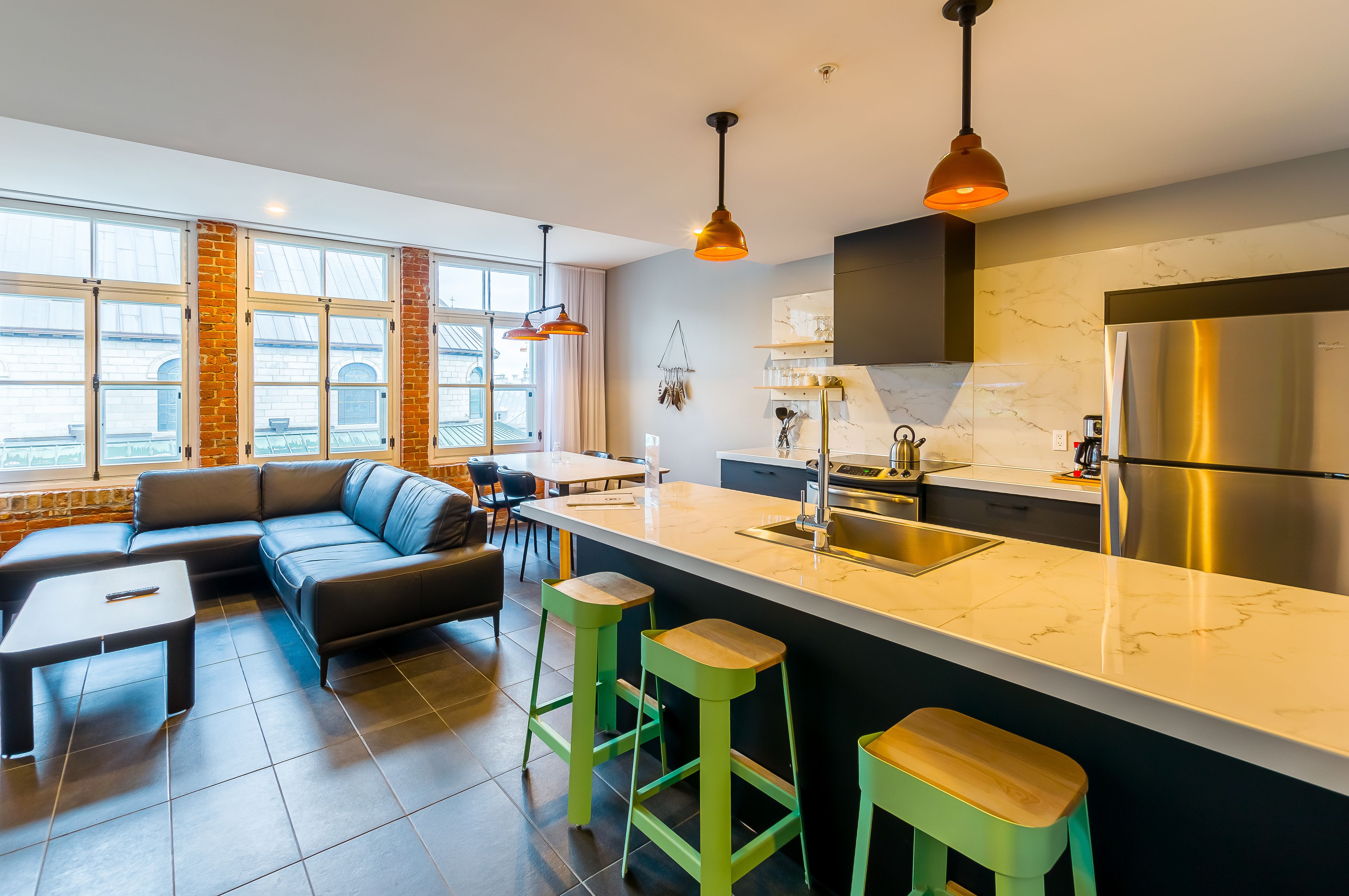 Una cocina moderna con una isla grande, electrodomésticos de acero inoxidable y una zona de estar con sofá y taburetes de bar.