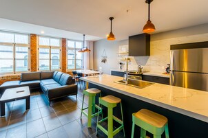 Una cocina moderna con una isla grande, electrodomésticos de acero inoxidable y una zona de estar con sofá y taburetes de bar.