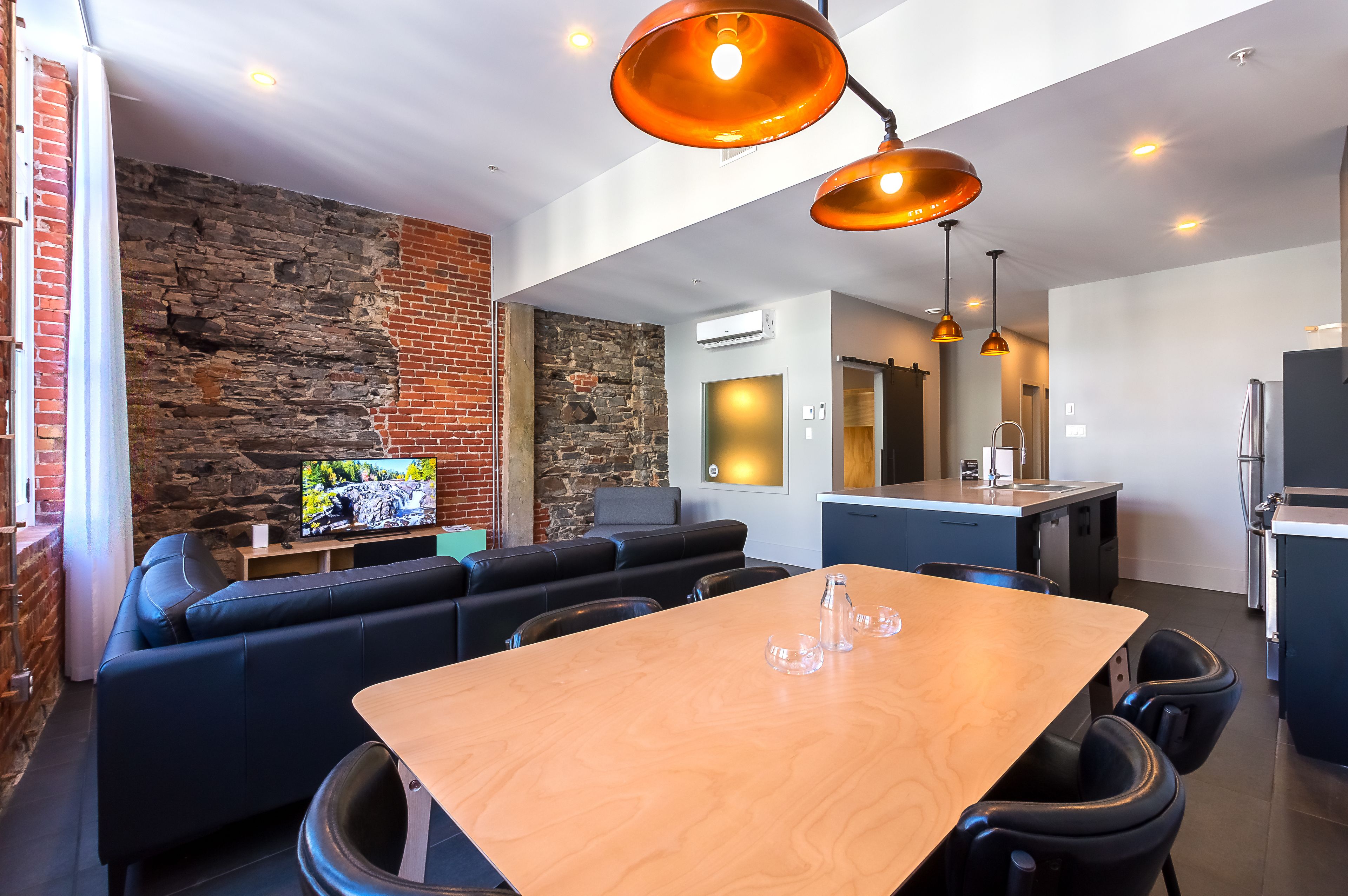 Un espacio habitable moderno con pared de piedra, sofá de cuero negro, mesa de comedor de madera y una zona de cocina.