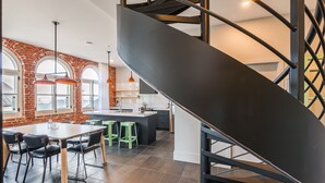Una cocina moderna con una isla central, una zona de comedor con sillas y una escalera que conduce a un nivel superior.