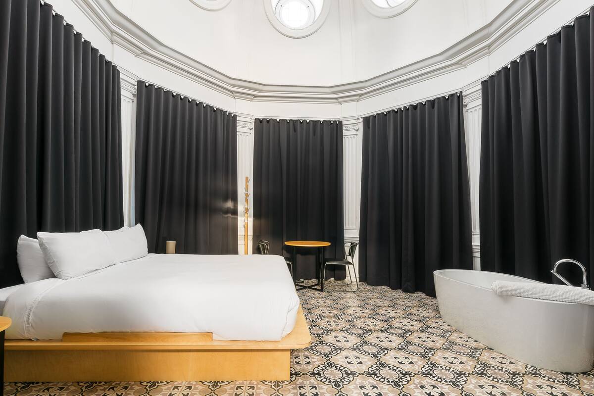 Ein Hotelzimmer mit einem großen Bett, einer Badewanne, einem kleinen runden Tisch und einem Sessel.