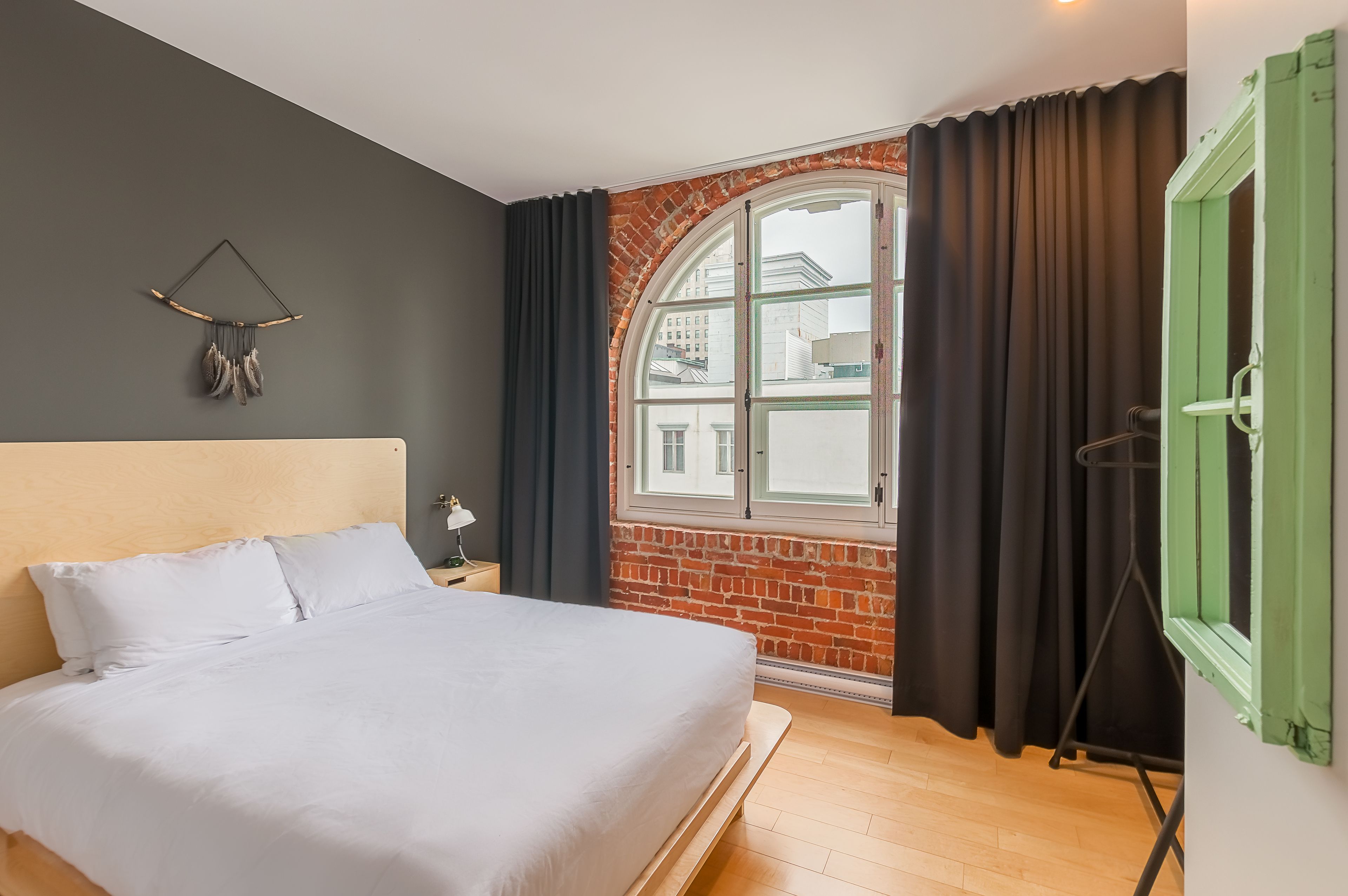 A bedroom with a large bed, a brick wall, a window with curtains, and a green door.