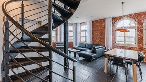 Una sala de estar moderna con una escalera curva, un sofá de cuero, una mesa de comedor y una pared de ladrillo.