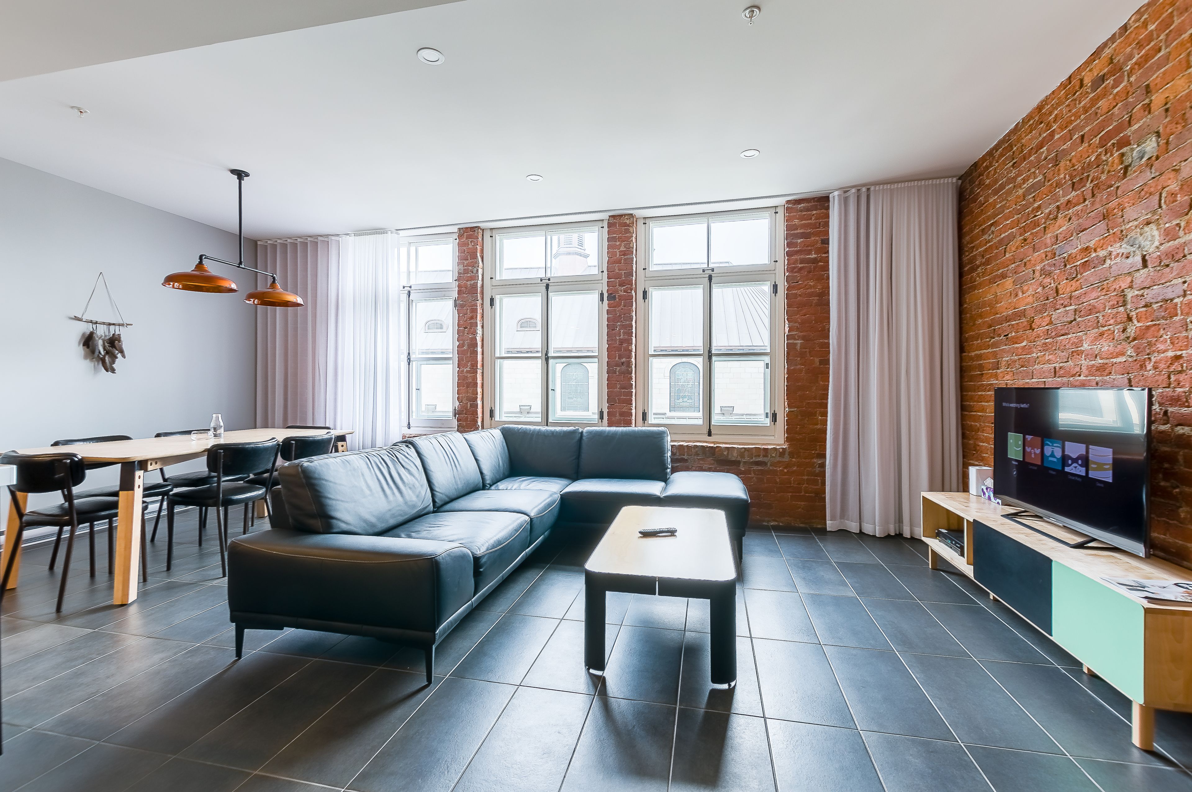 Uma sala de estar moderna com um sofá seccional, uma mesa de centro, uma TV sobre um suporte de madeira e uma área de jantar com mesa e cadeiras.
