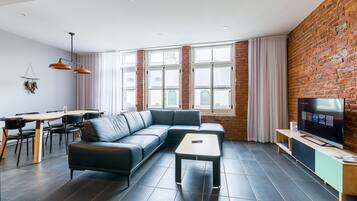 Uma sala de estar moderna com um sofá seccional, uma mesa de centro, uma TV sobre um suporte de madeira e uma área de jantar com mesa e cadeiras.