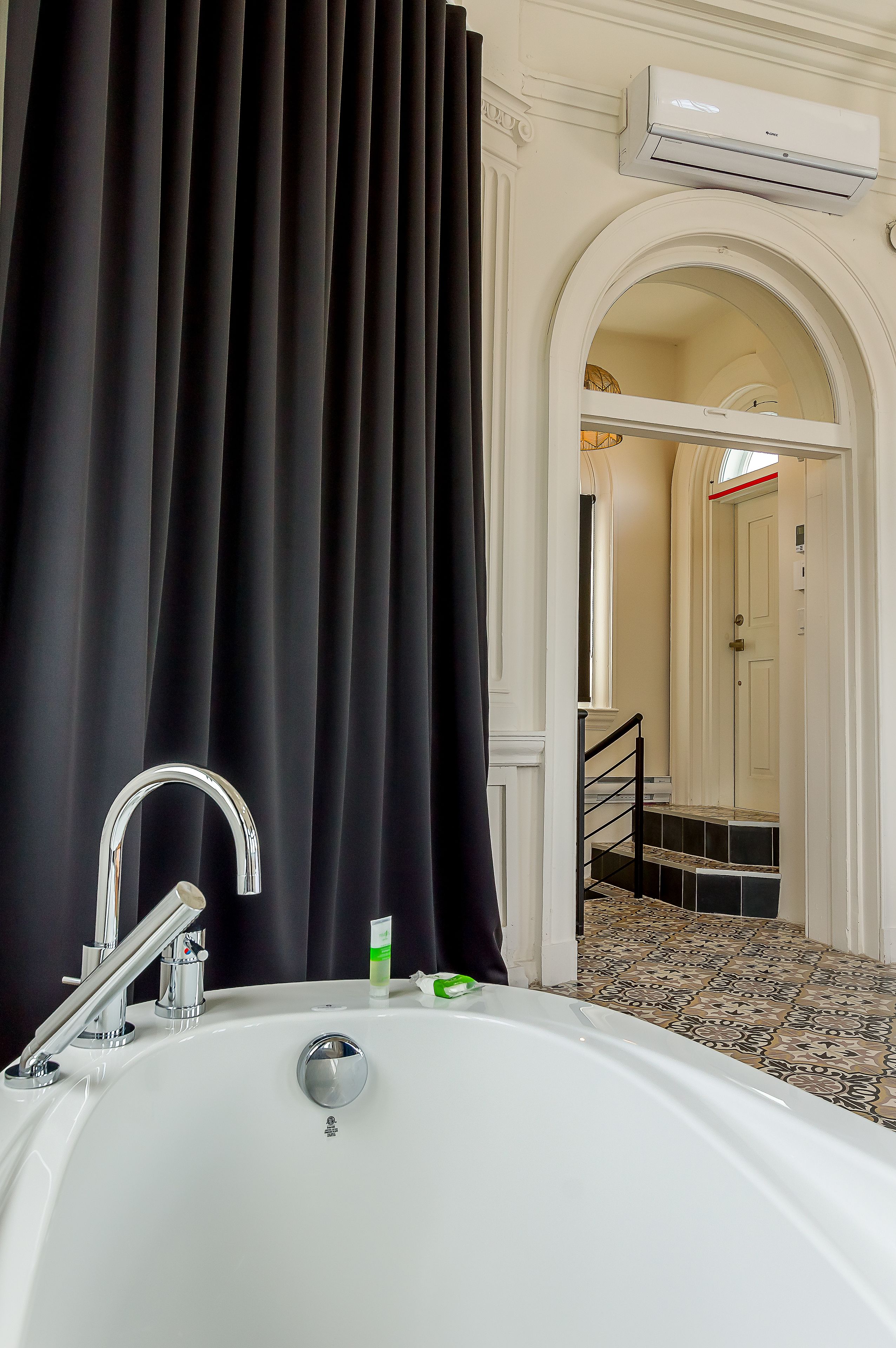 Ein Badezimmer mit Badewanne, Dusche und Toilette. Ein schwarzer Vorhang, ein weißes Waschbecken und ein gefliester Boden sind vorhanden.