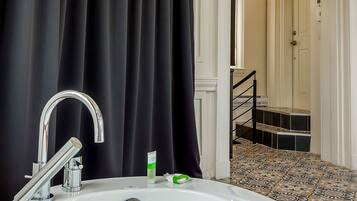 Un baño con bañera, ducha e inodoro. Hay una cortina negra, un lavamanos blanco y un suelo de baldosas.