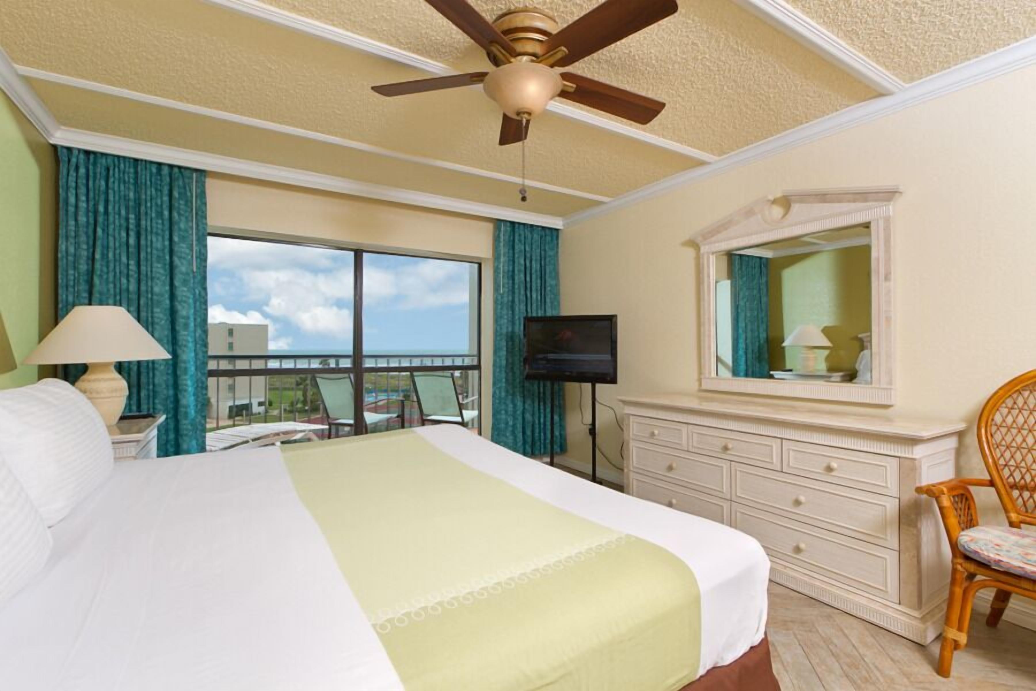 Une chambre d’hôtel avec un grand lit, un ventilateur de plafond, une télévision, une commode et une fenêtre donnant sur l’extérieur.