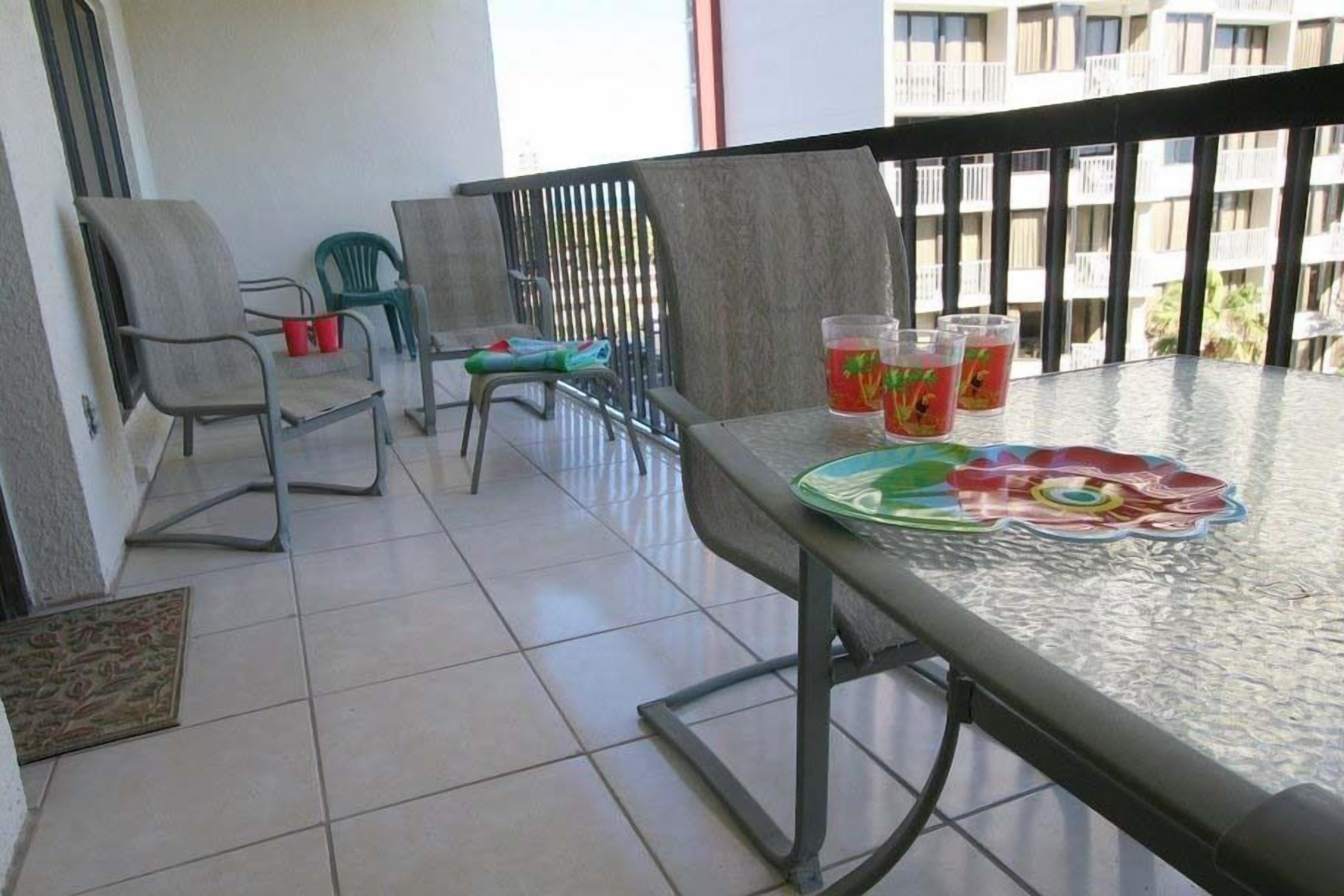 A balcony with a glass table, chairs, and a view of a building.